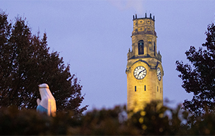 The clocktower on Detroit Mercy's McNichols Campus, shown at night, with a religious statue in the foreground.