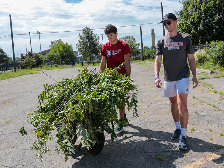 A pair of students move limbs and brush away on a wheelbarrow near Detroit Mercy's McNichols Campus.