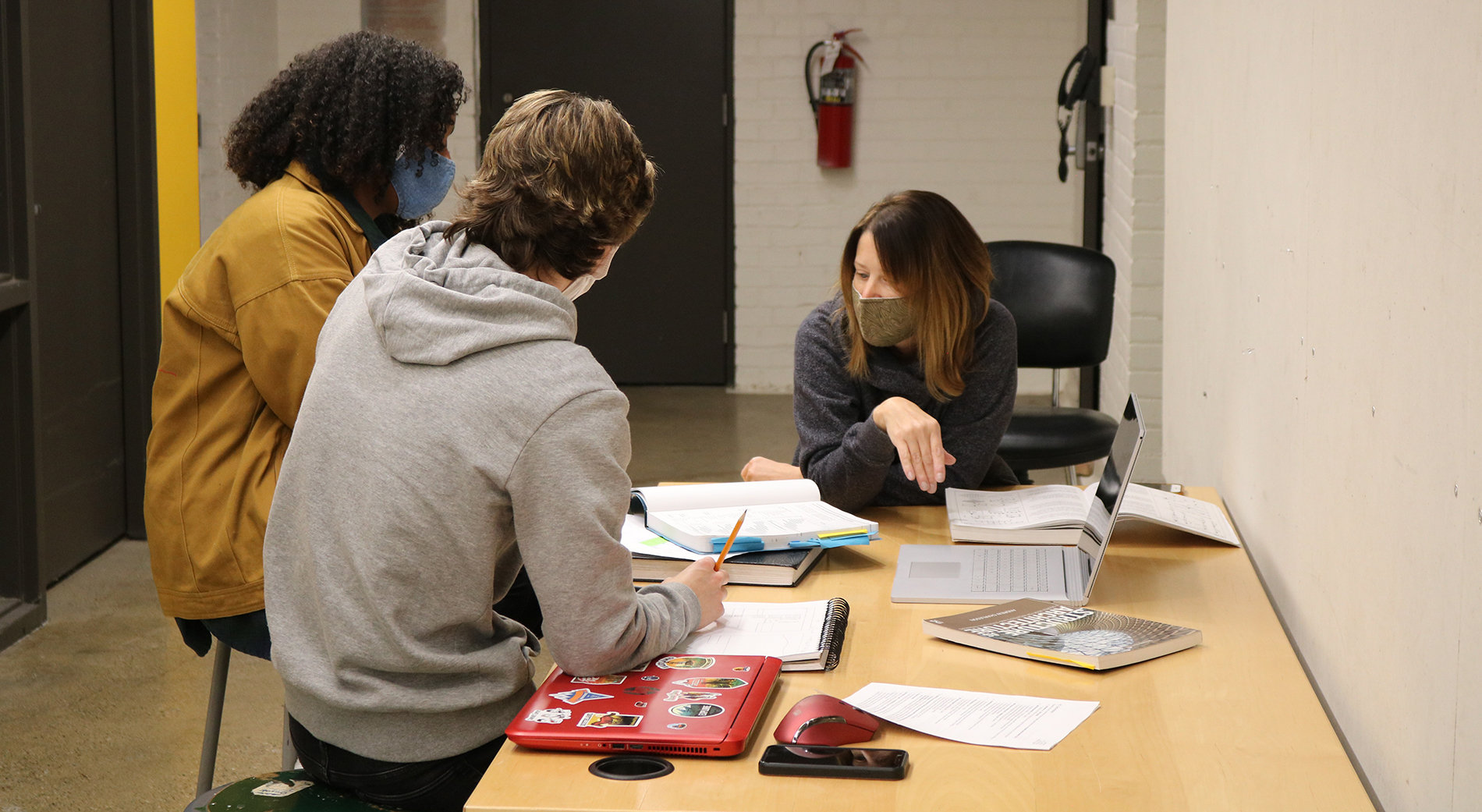 A faculty member helps students with coursework at one of the desks inside the Loranger Architecture building.