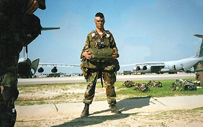 A photo of Mike Norris at a military base. Several aircrafts and equipment are in the background.