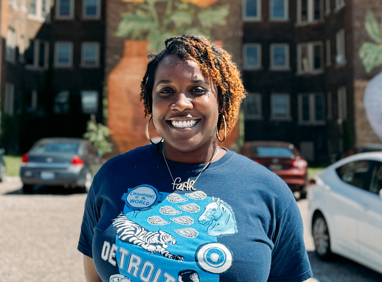 Bethany Walls stands outdoors in front of buildings and cars.