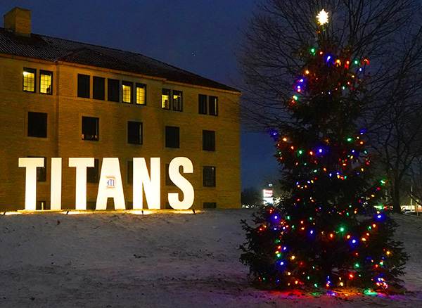 TITANS is lit up on the McNichols Campus, which also features a colorful Christmas tree and Holden Hall on a snowy evening.