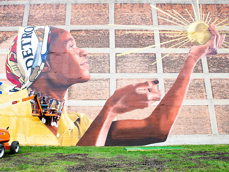 A mural painting in Detroit depicts a woman holding the Spirit of Detroit on a brick wall.