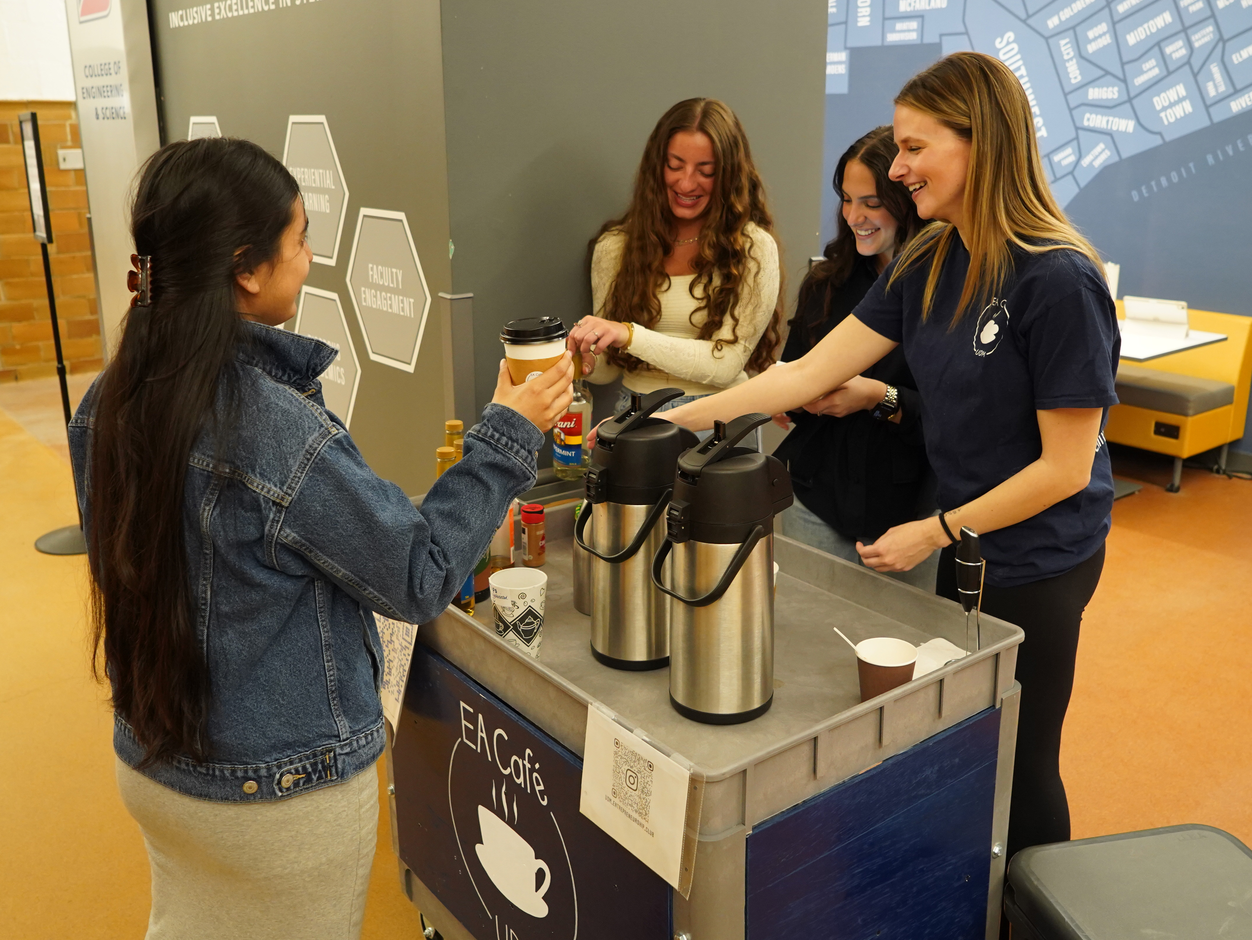 Four students stand around the EA Cafe coffee cart, inside of the Engineering Building.