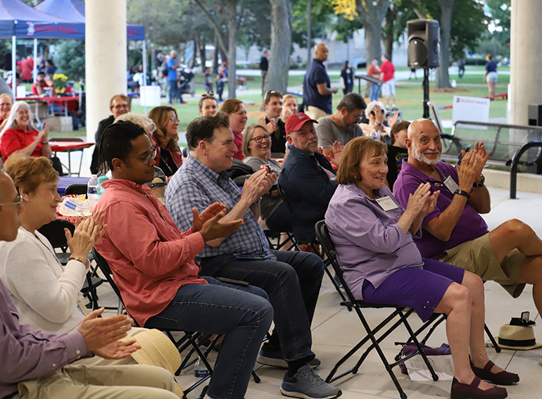 More than a dozen people sit and clap and laugh during a performance at Homecoming on the McNichols Campus.