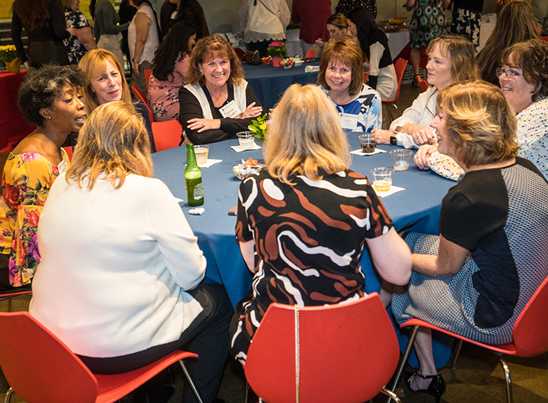 Nine people sit around a table indoors during a Homecoming event.