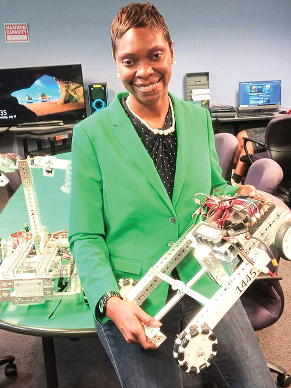 Dee Pearl stands holding a mechanical design inside of a computer lab.