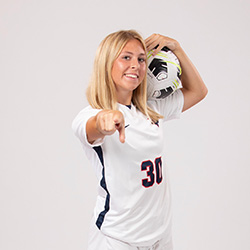 A photo of Mya Mascaro holding a soccer ball and pointing.