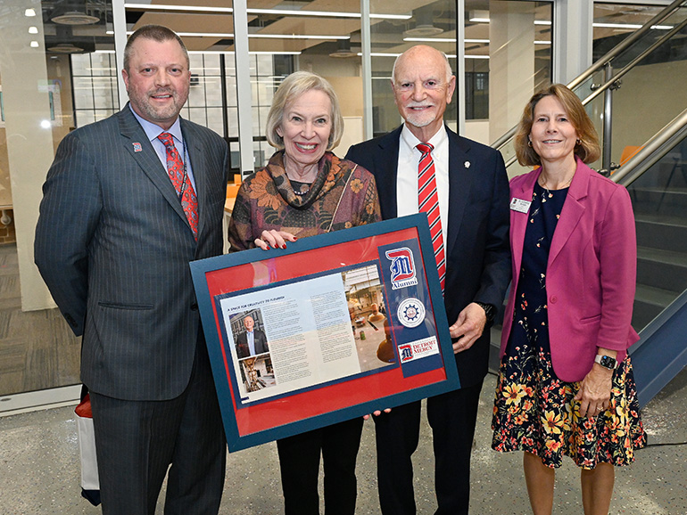 Four people stand and pose for a photo inside of the High Bay, one holding a picture frame.