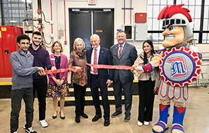 Eight people and a mascot cut a ribbon inside of an annex.