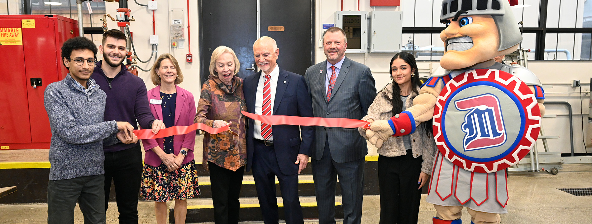 Eight people and a mascot cut a ribbon inside of an annex.