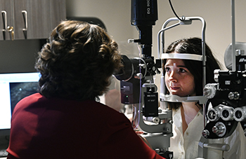 A woman exams another woman's eyes during an eye examination.