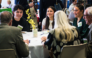 Students and scholarship donors sit around a table and mingle at a reception event.