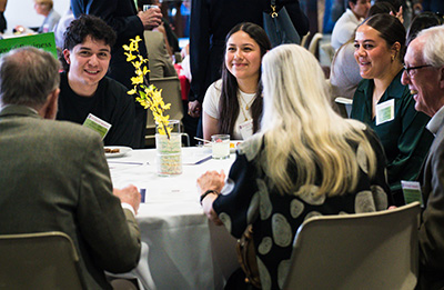 Students and scholarship donors sit around a table and mingle at a reception event.