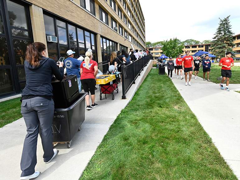 People push belongings up towards Shiple Hall, with others walking down the sidewalk outdoors.