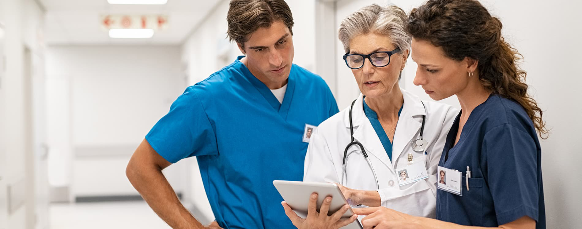 Three healthcare professionals stand close together while viewing a tablet.