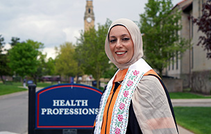 Shreen Marini stands outside the Health Professions Building at UDM with the clocktower in the background.