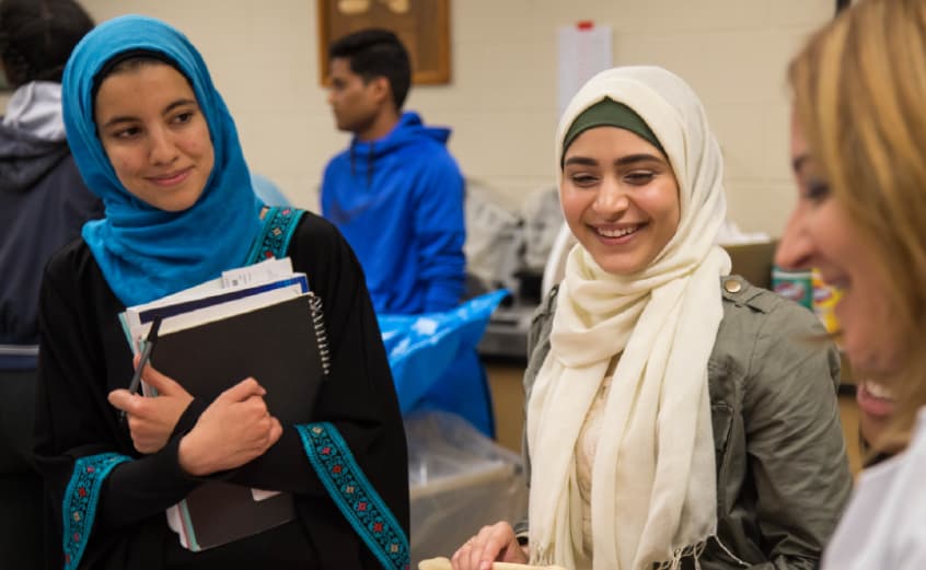 two students in hijabs smiling and carrying their books