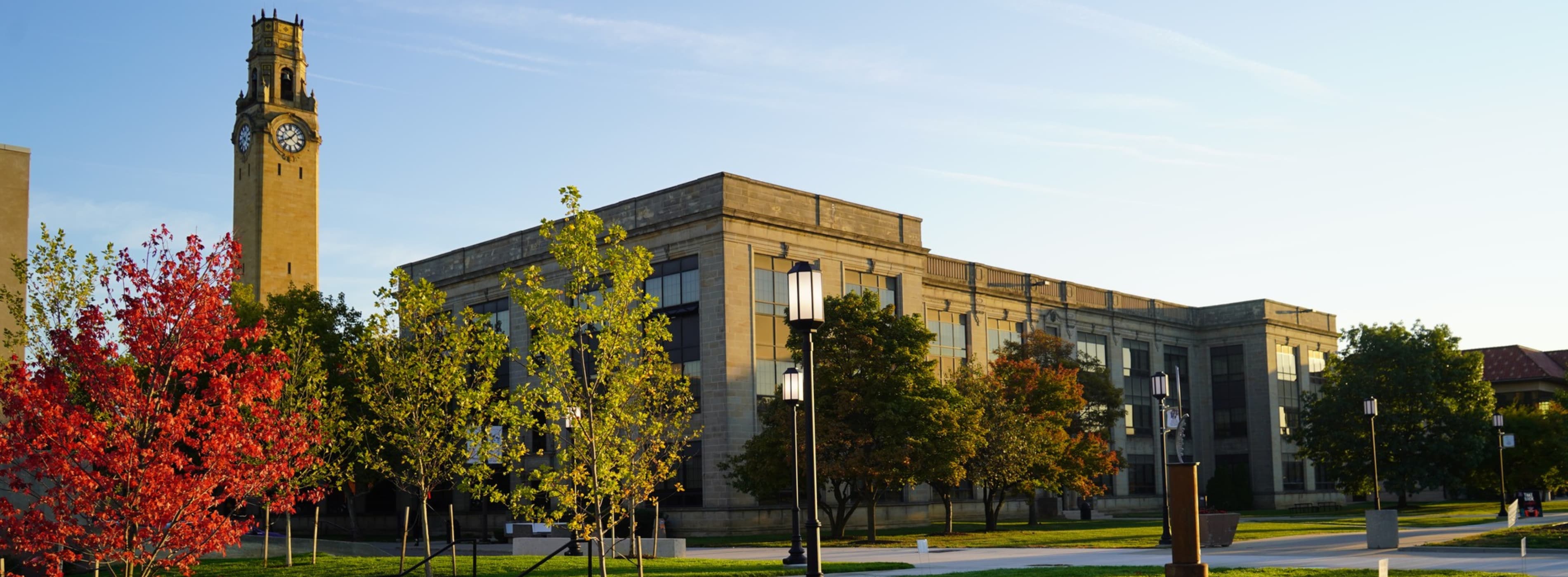 The clocktower and an academic building are seen on a fall day.