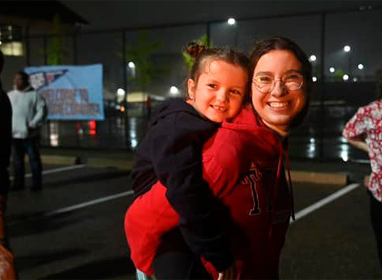 alumni mother and her child on her back at the bonfire