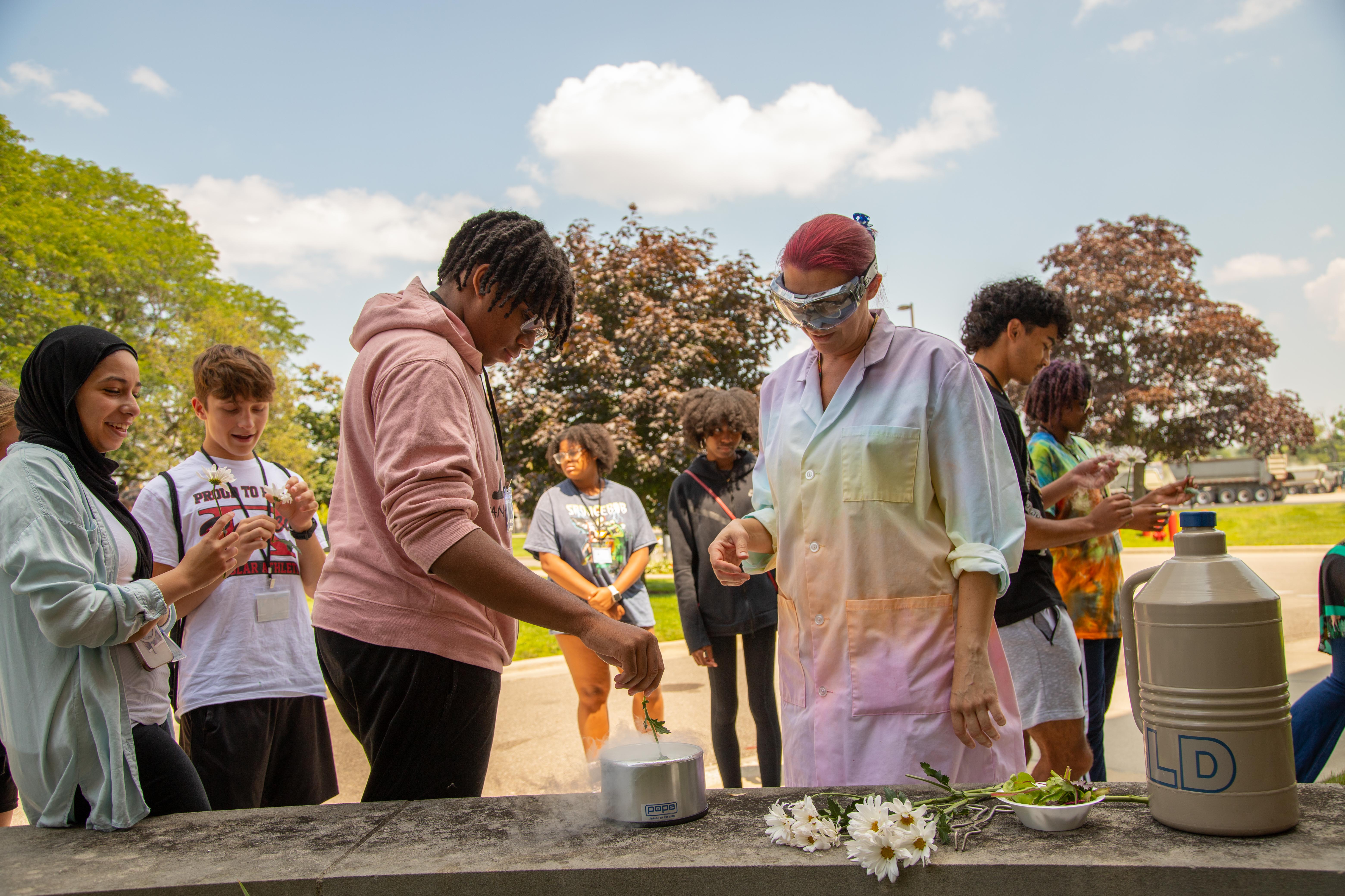 An instructor with seven students participate in a science activity featuring flowers outdoors on a sunny day.