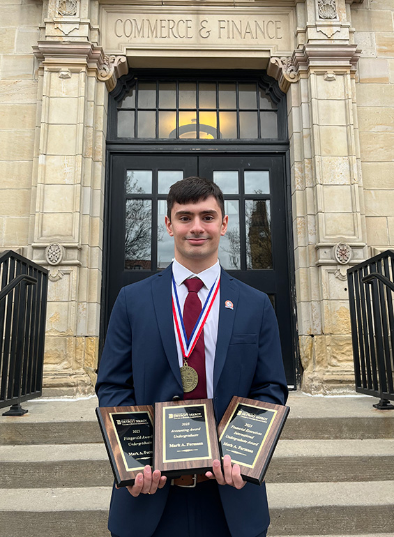 Mark Formosa stands in front of the Commerce & Finance Building while holding a number of awards.