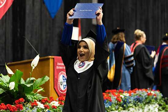 Detroit Mercy student holds up her diploma in excitement.