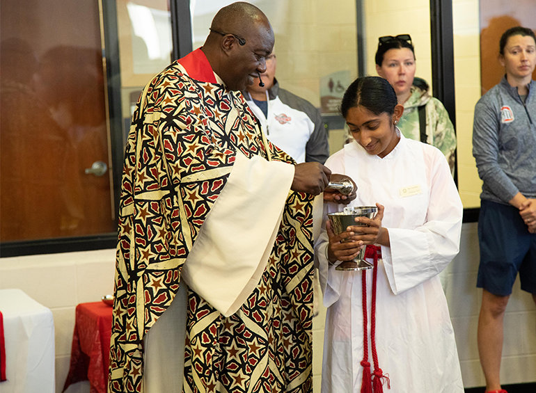 An image of Fr. Oduke blessing the chalice of wine held by a altar server